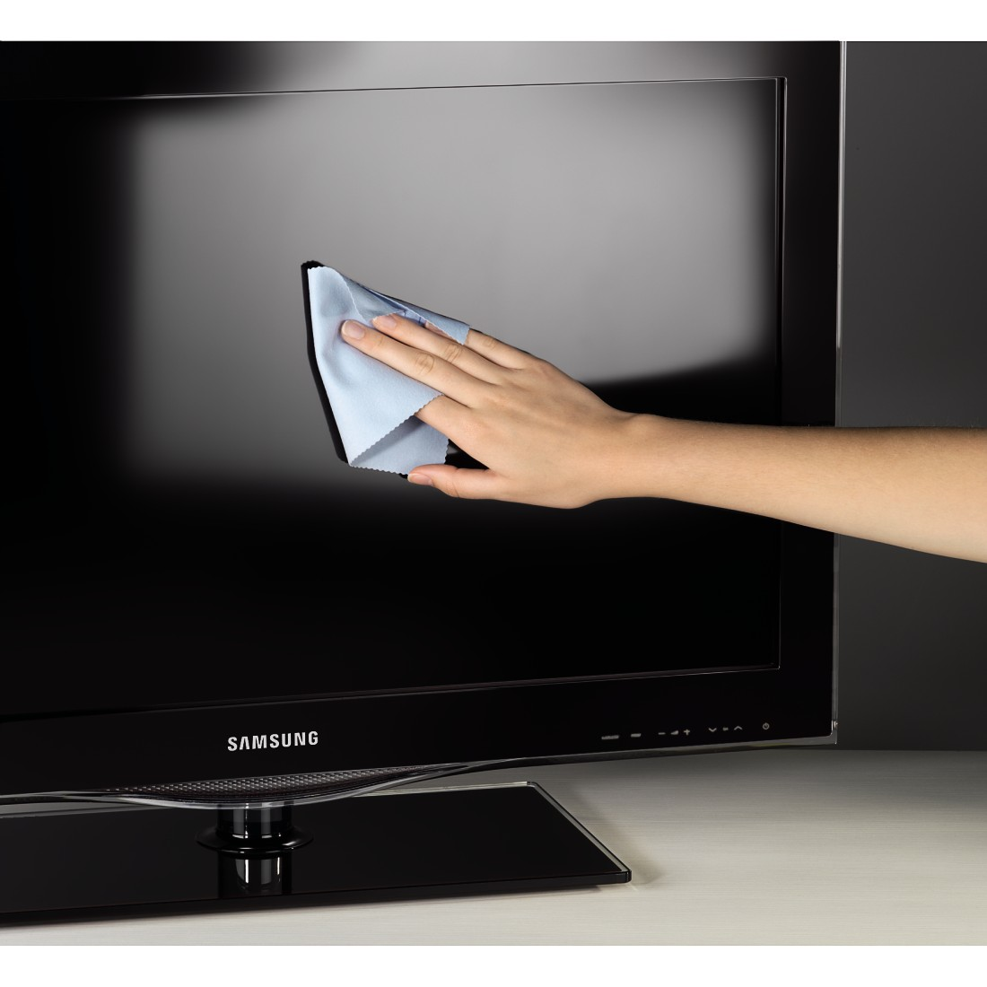 Die Hand einer Person reinigt einen schwarzen Fernsehbildschirm mit einem blauen Tuch.