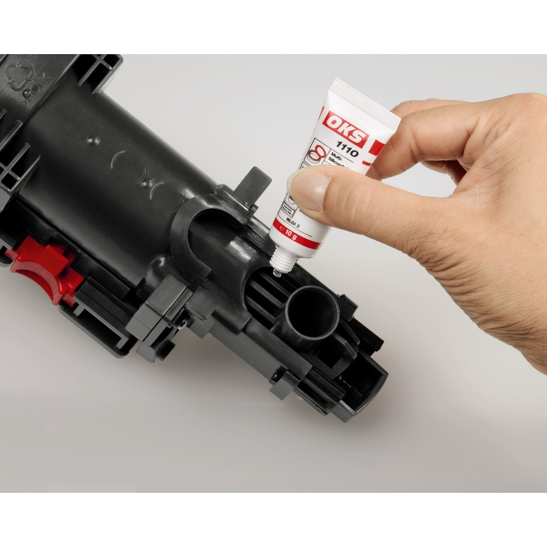 A hand squeezing white cream from a tube into a black machine component.