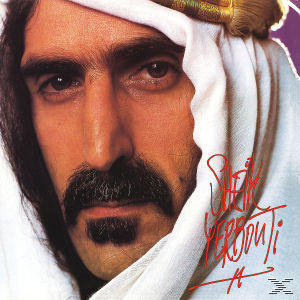 Nahaufnahme von Frank Zappa in arabischer Kleidung, mit weißem Kopftuch und Schnurrbart, der in die Kamera schaut.