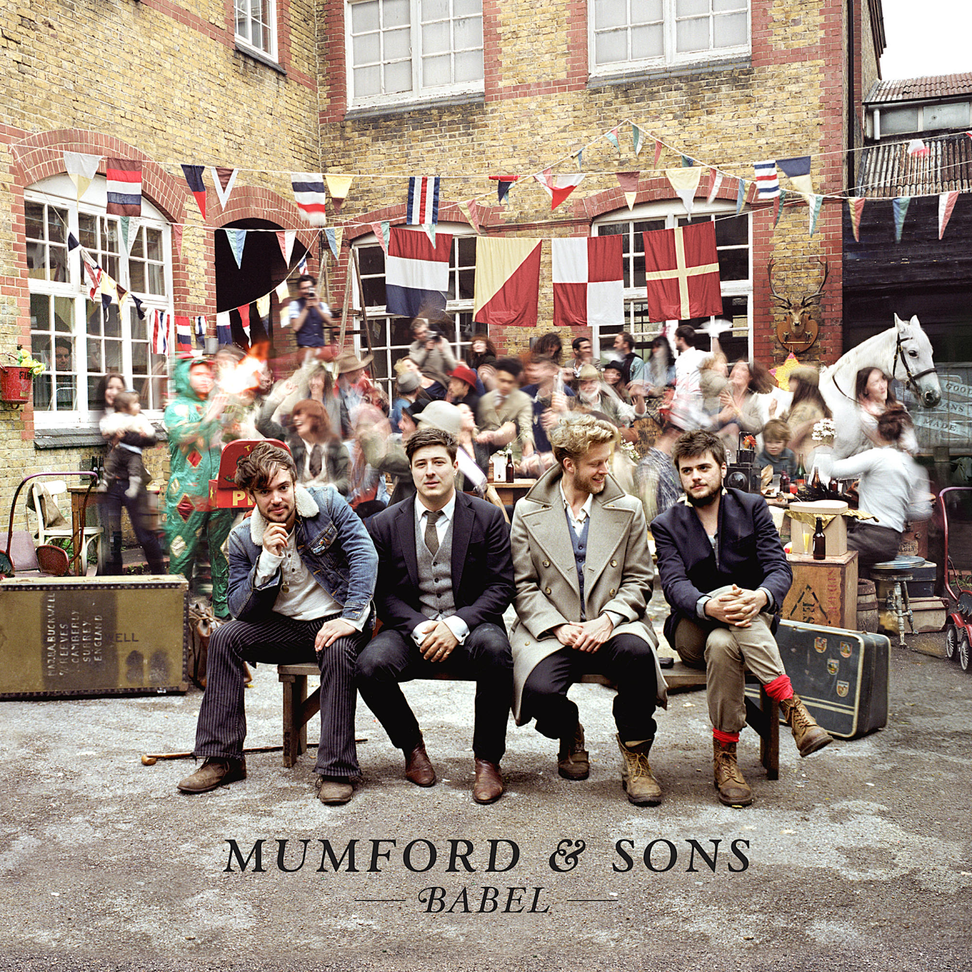 Mumford & Sons Albumcover. Vier Männer sitzen. Im Hintergrund eine belebte Straße mit Fahnen und Menschen.