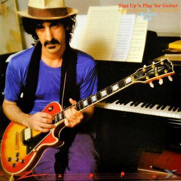 Mann mit Gitarre. Er trägt einen Hut und ein blaues Hemd. Die Gitarre hat gelbe und rote Farben. Im Hintergrund ein Klavier.