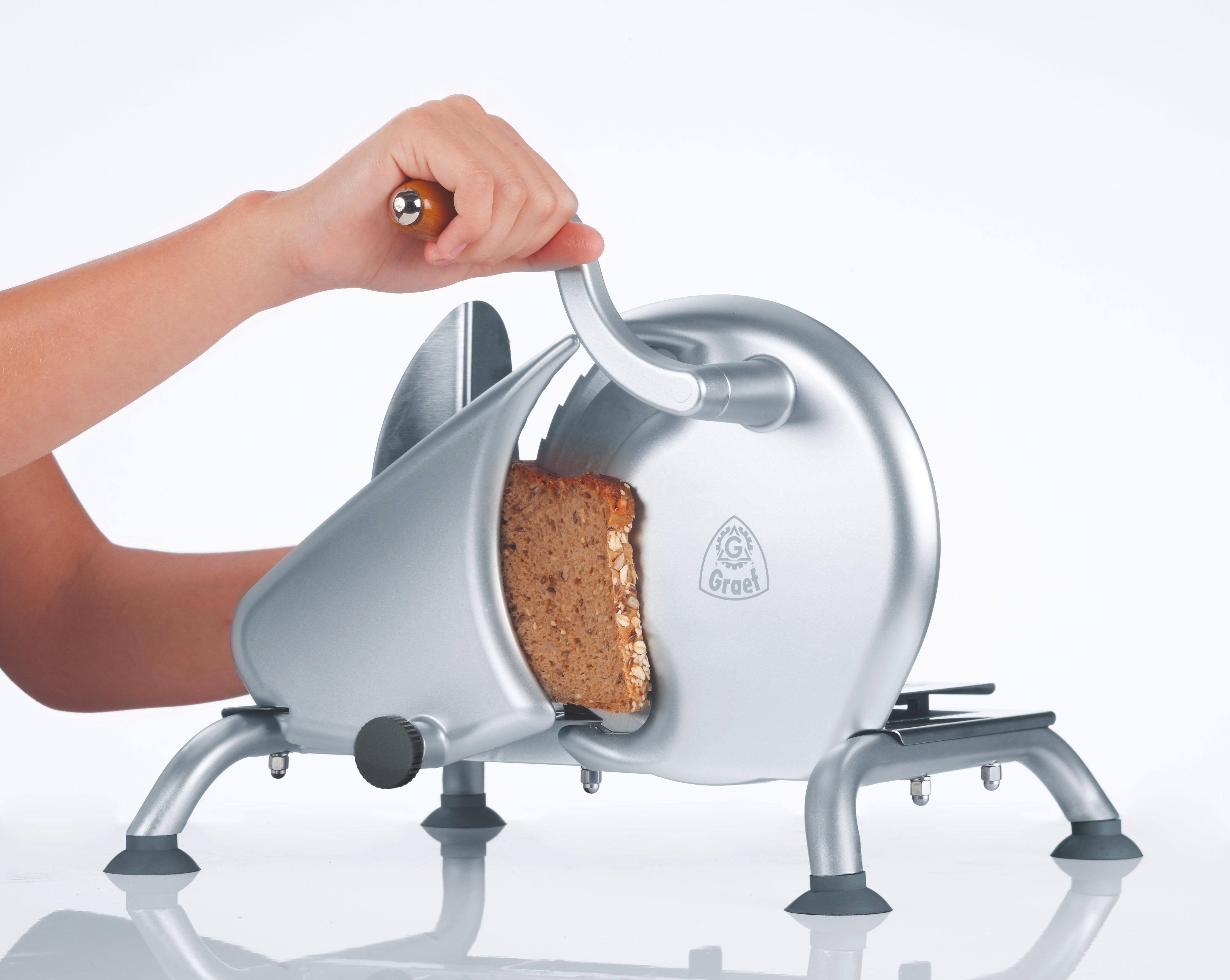 Eine Person schneidet Brot mit einem silbernen Graef-Schneider. Das Brot wird in Scheiben geschnitten.