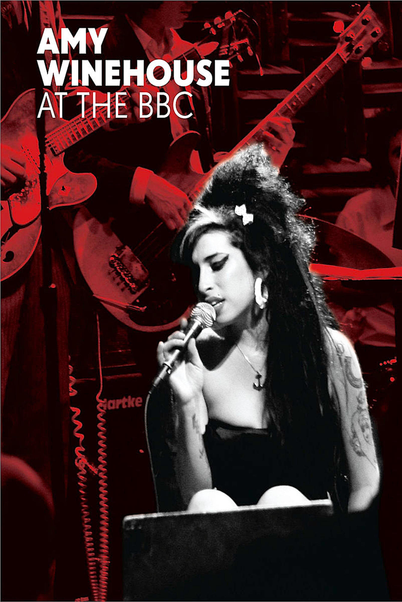 Amy Winehouse singt in ein Mikrofon, mit Bandmitgliedern im Hintergrund.