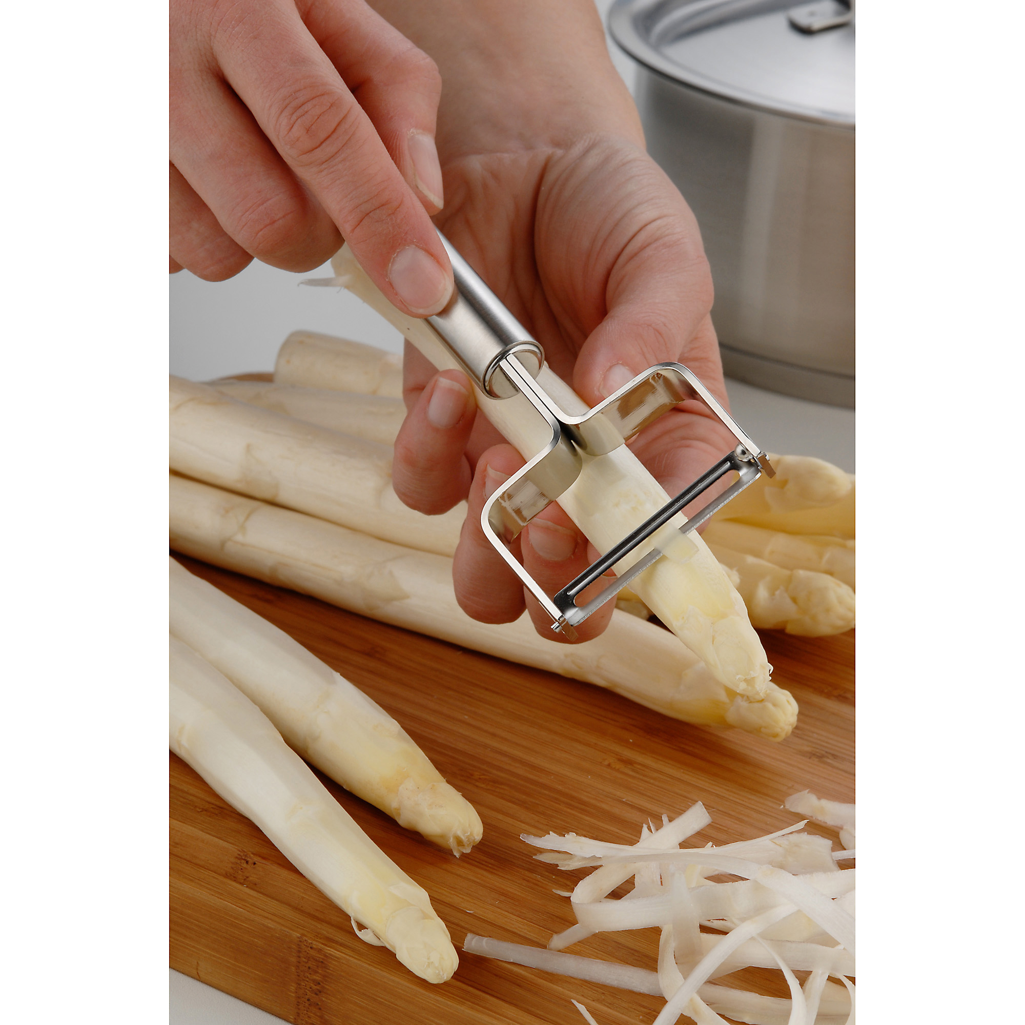 Hände schälen Spargel mit einem Schäler. Spargelstangen und Späne auf Holzbrett.