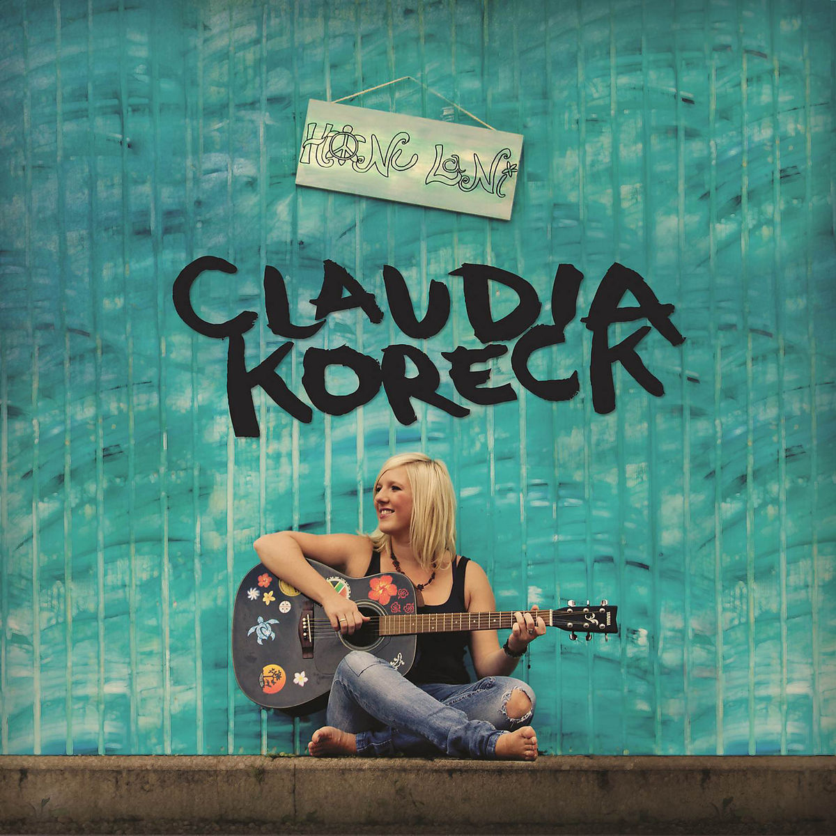 Claudia Koreck Albumcover: Eine Frau mit Gitarre sitzt vor einer türkis bemalten Wand mit ihrem Namen.
