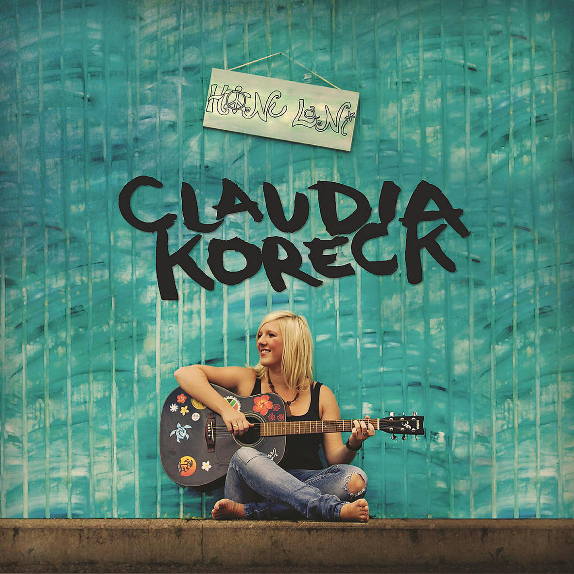 Blonde Frau mit Gitarre vor türkisfarbener Wand.