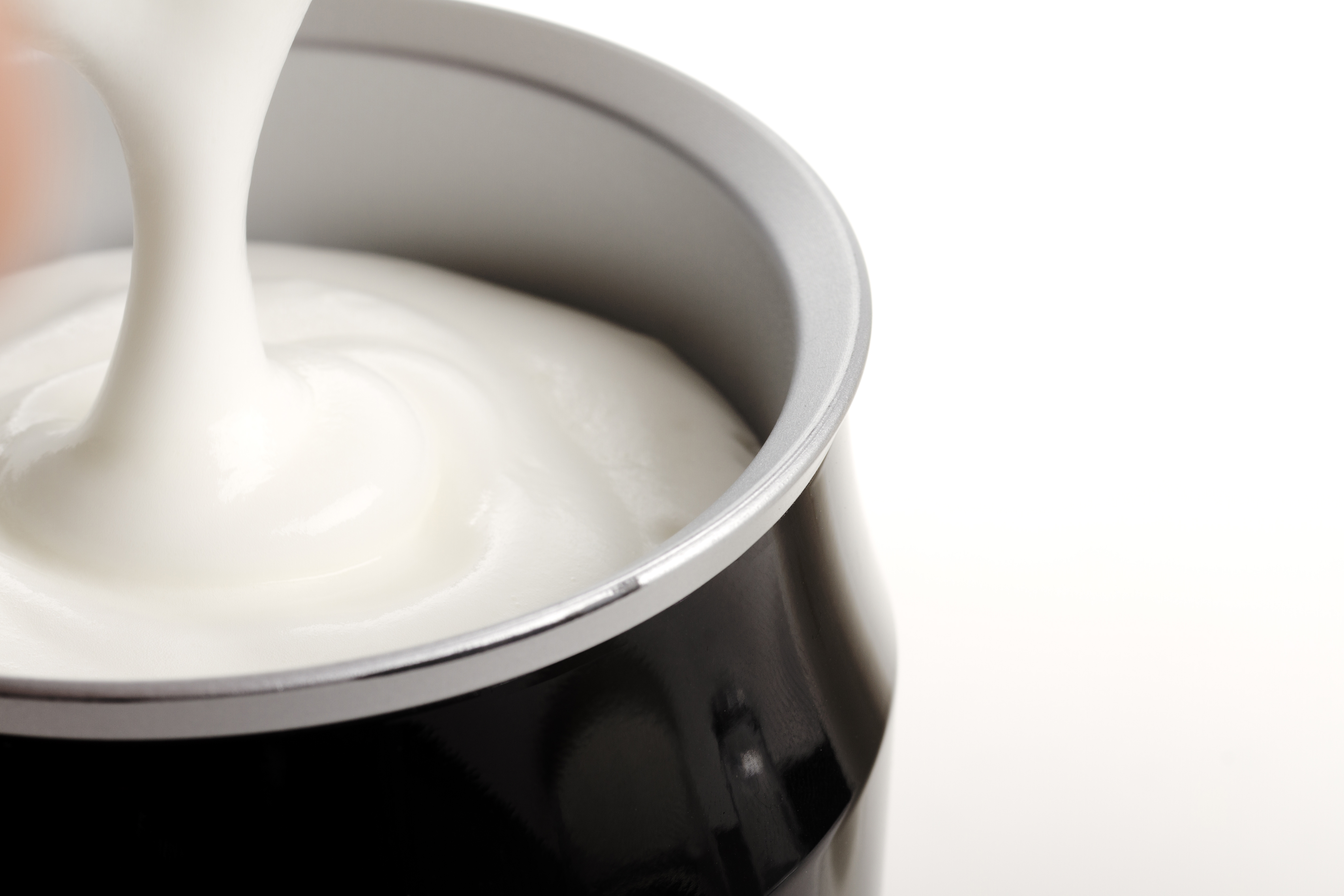 Nahaufnahme von weißer Creme, die aus einem schwarzen Behälter gegossen wird.