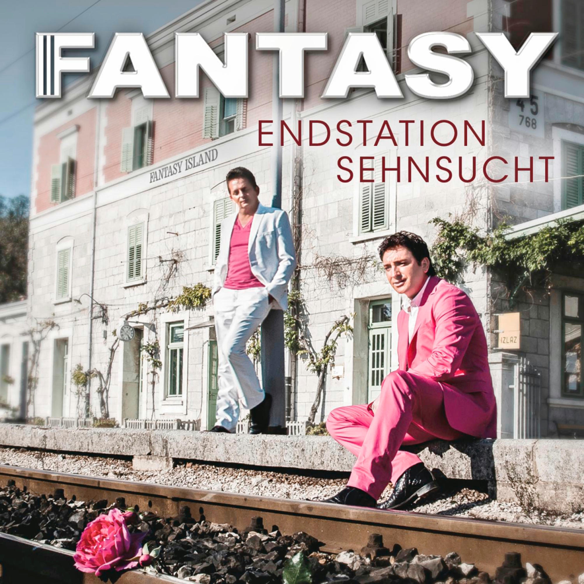 Zwei Männer in Anzügen posieren an Bahngleisen. Einer in Weiß, einer in Rosa. Der Titel lautet "FANTASY ENDSTATION SEHNSUCHT".