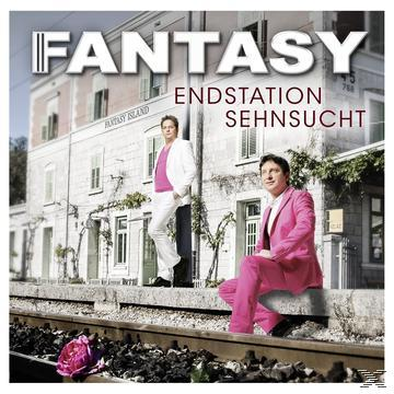 Zwei Männer in Anzügen stehen und sitzen in der Nähe eines Gebäudes mit dem Wort 'FANTASY'.