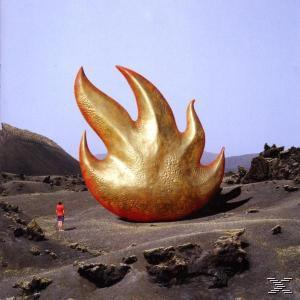 Albumcover mit einer großen goldenen Flammenskulptur in einer kargen Landschaft und einem Mann in der Ferne.