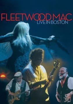 Fleetwood Mac live auf der Bühne. Bandmitglieder spielen Instrumente, im Hintergrund eine Frauensilhouette.