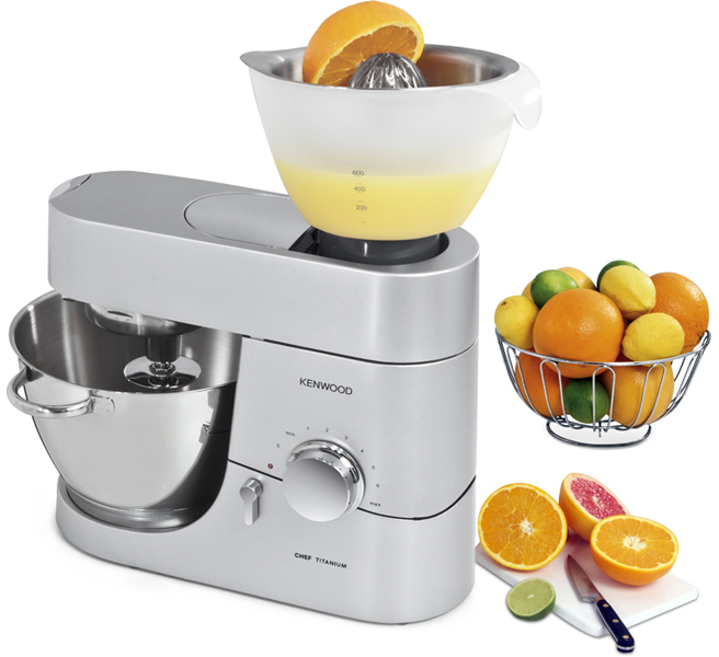 Küchengerät. Silberner Mixer mit Entsafteraufsatz. Orangen, Limetten und ein Messer auf weißer Oberfläche.