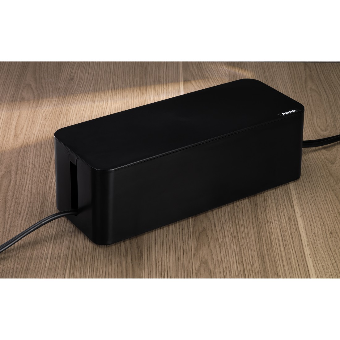 Schwarze Kabelmanagementbox auf Holzoberfläche, Kabel kommen heraus.