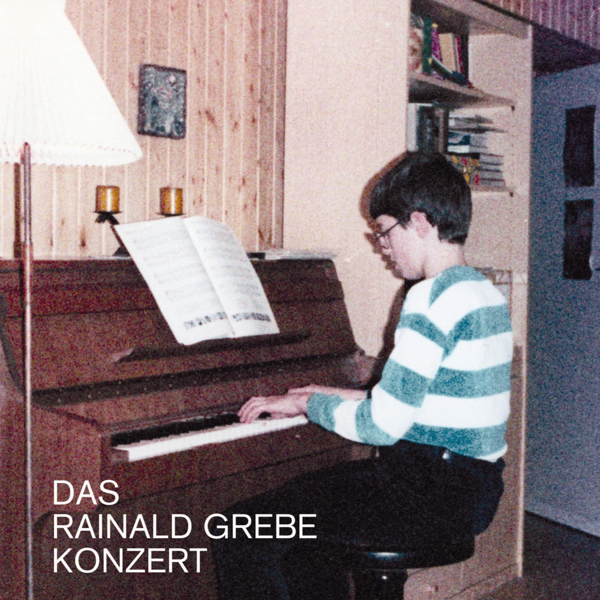Ein Junge spielt Klavier, Noten, Holzvertäfelung, Lampe und Text: Das Rainald Grebe Konzert.