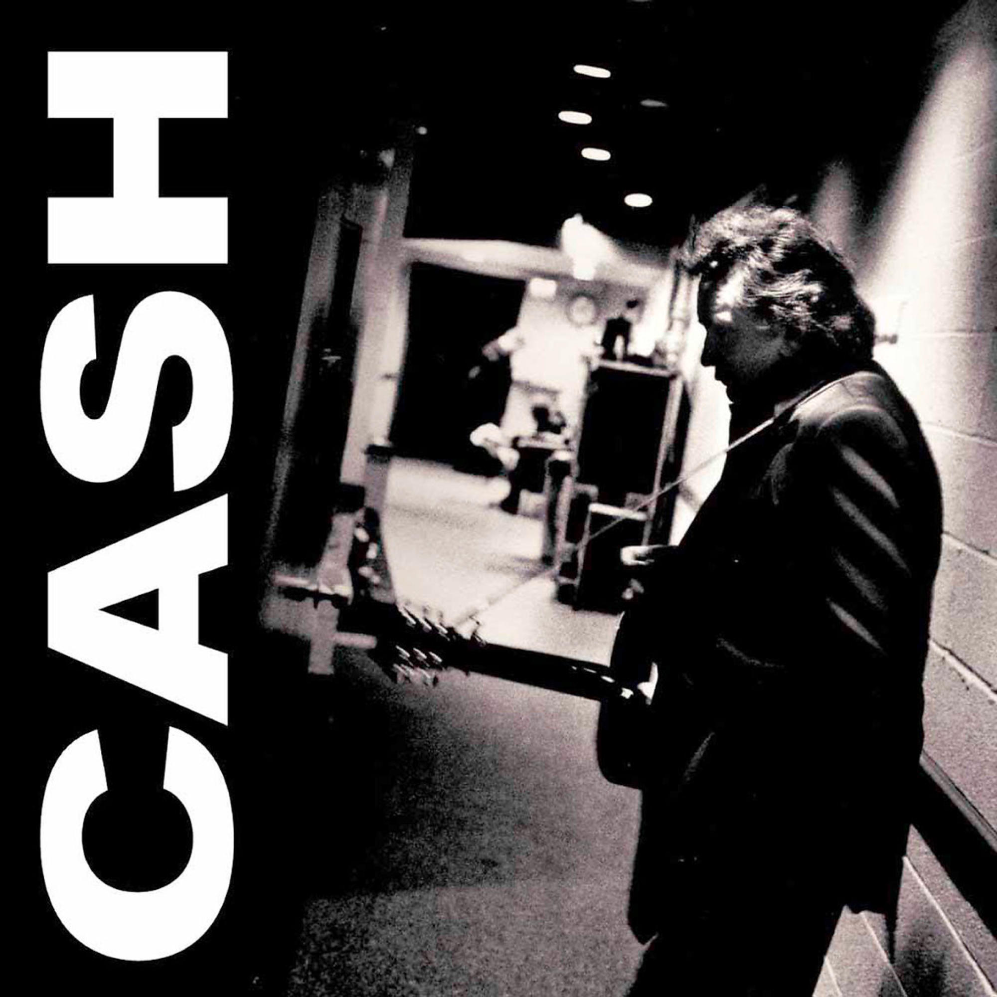 Cash Musikalbum-Cover. Johnny Cash spielt Gitarre in einem schattigen Flur. Großer weißer 'CASH'-Text.