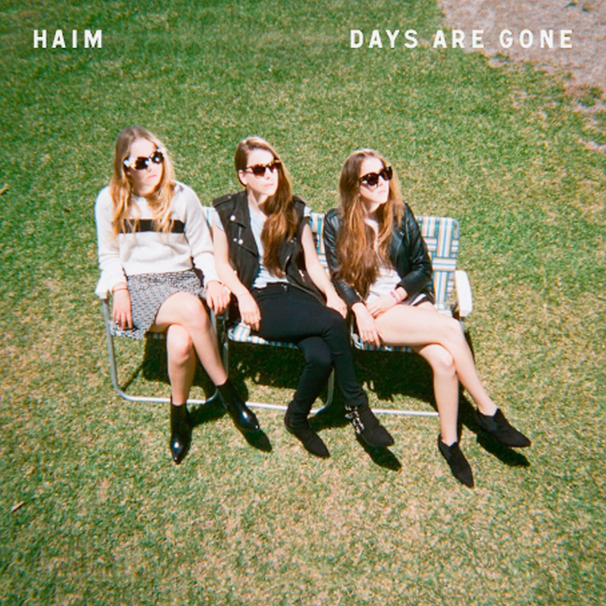 HAIM Band-Albumcover. Drei Frauen mit Sonnenbrillen sitzen auf einer Parkbank auf grünem Gras.