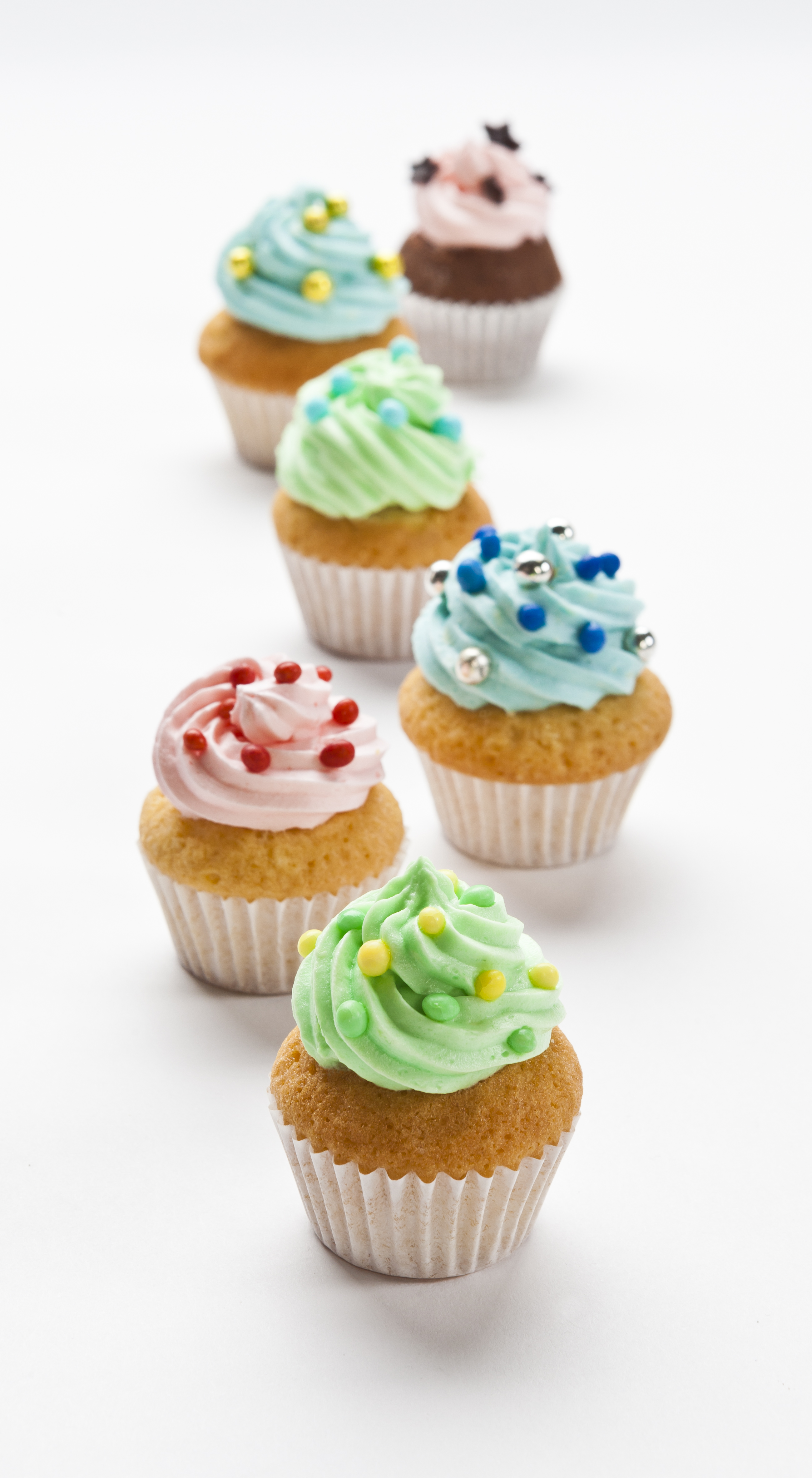 Reihe Cupcakes, verschiedene Farben Zuckerguss und Streusel. Weißer Hintergrund.