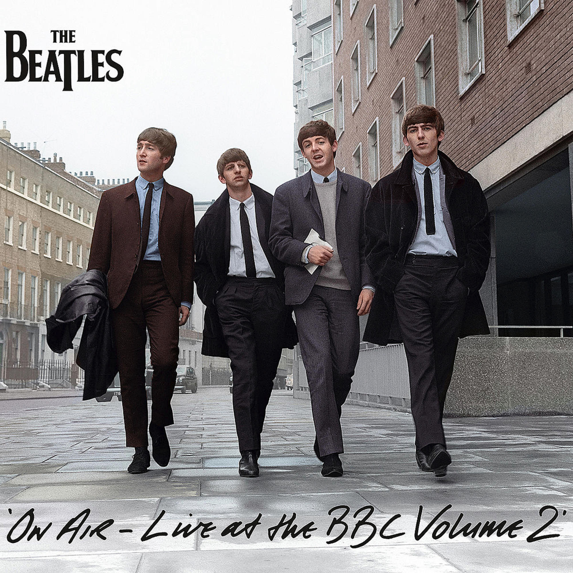 Die Beatles gehen auf einer Straße, mit Gebäuden und Schild im Hintergrund.