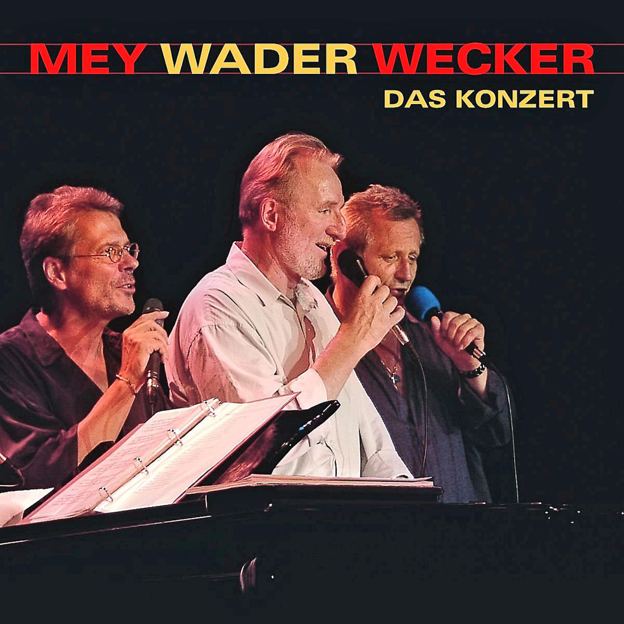 Konzertplakat mit drei Männern auf der Bühne, die in Mikrofone singen. Der Titel lautet 'Mey Wader Wecker' und 'Das Konzert'.