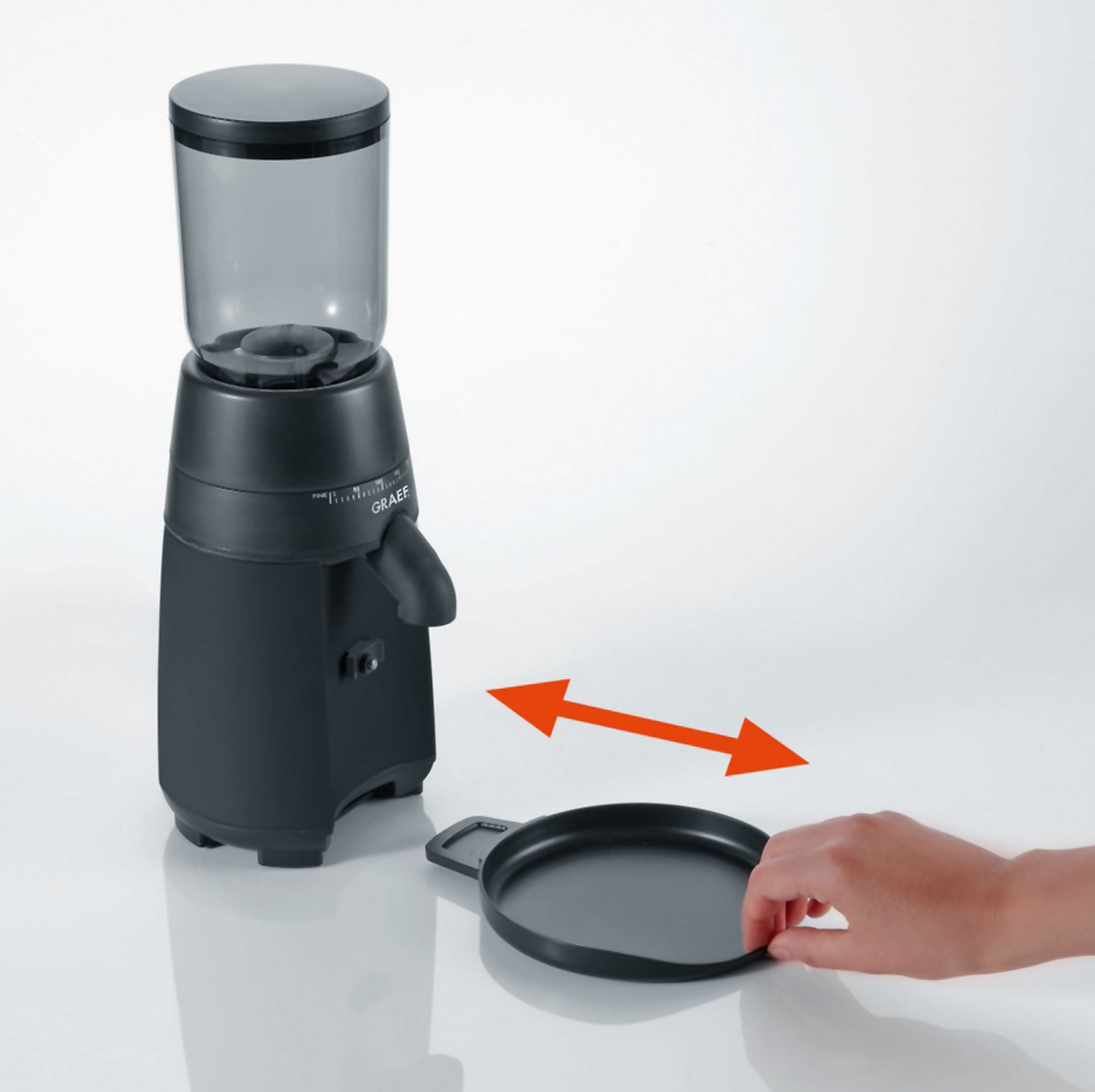 Schwarze Kaffeemühle mit einer Hand, die eine schwarze Ablage hält, mit Pfeil.