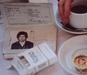 Reisepass mit Foto von Bob Dylan. Zigarettenschachtel, Kaffeetasse und Untertasse auf Holztisch.