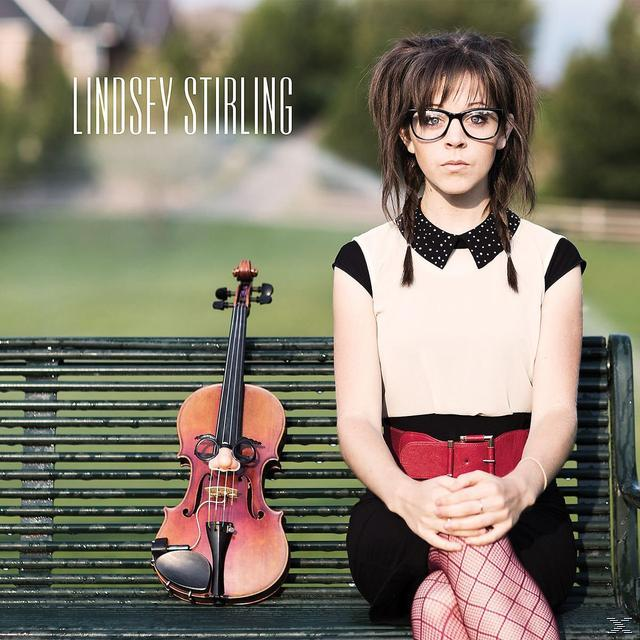 Lindsey Stirling sitzt mit einer Geige auf einer Parkbank. Sie trägt eine Brille, einen Polka-Dot-Kragen und rot gemusterte Strümpfe.