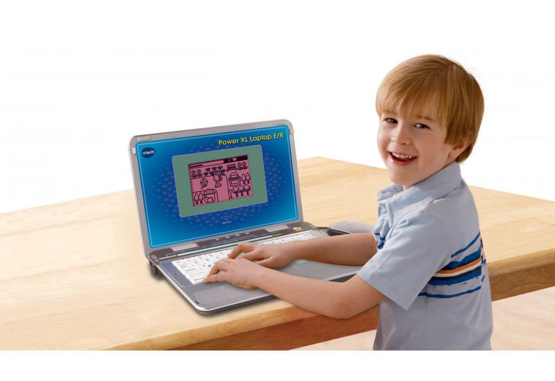 Junge benutzt einen VTech-Laptop auf einem Holztisch und lächelt in die Kamera.