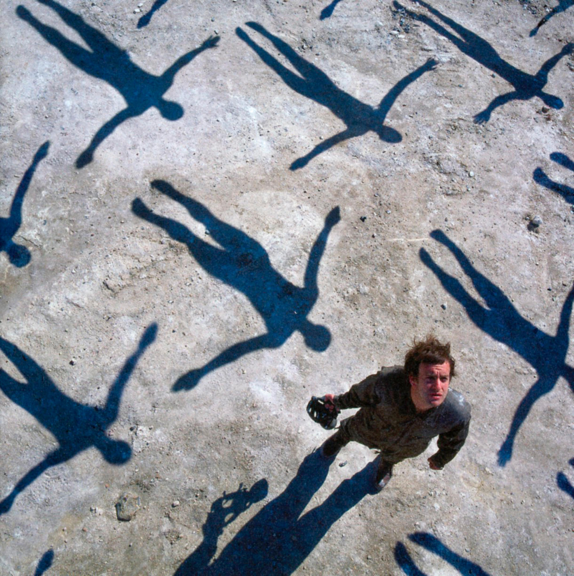 Ein Mann, der nach oben schaut, mit Schatten von Figuren, die wie fallende Menschen aussehen, auf einer hellen Oberfläche.