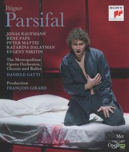 A 'Parsifal' opera plakátja. Egy férfi térdel az ágyon, kezét a mellkasán tartja, egy piros szobában.