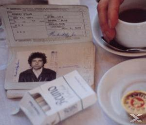 Reisepass von Bob Dylan, Zigaretten, Kaffee und ein Teller auf einem Tisch, mit einer Hand rechts.
