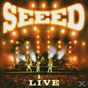 Albumcover der Band Seed, die auf der Bühne vor Publikum auftritt.