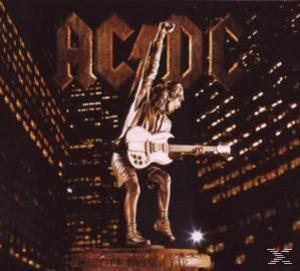 AC/DC-Statue, die vor einer Stadtkulisse Gitarre spielt.