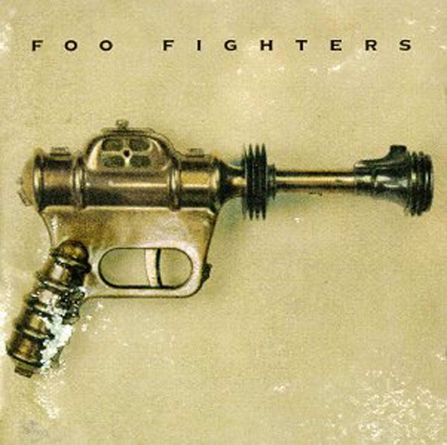 Albumcover für Foo Fighters mit einem metallischen, waffenartigen Objekt auf beigem Hintergrund.