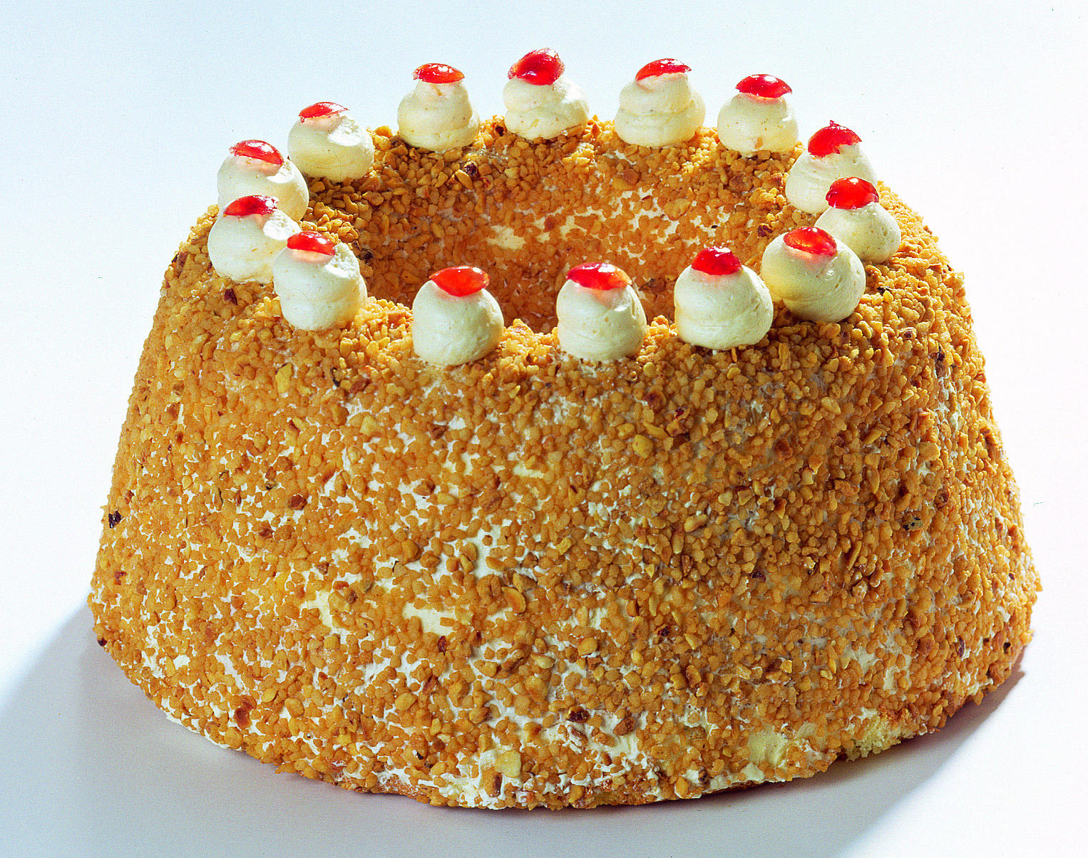 Ein runder Kuchen, bedeckt mit Nüssen, belegt mit Sahne und rotem Gelee. Der Kuchen steht auf einer weißen Oberfläche.