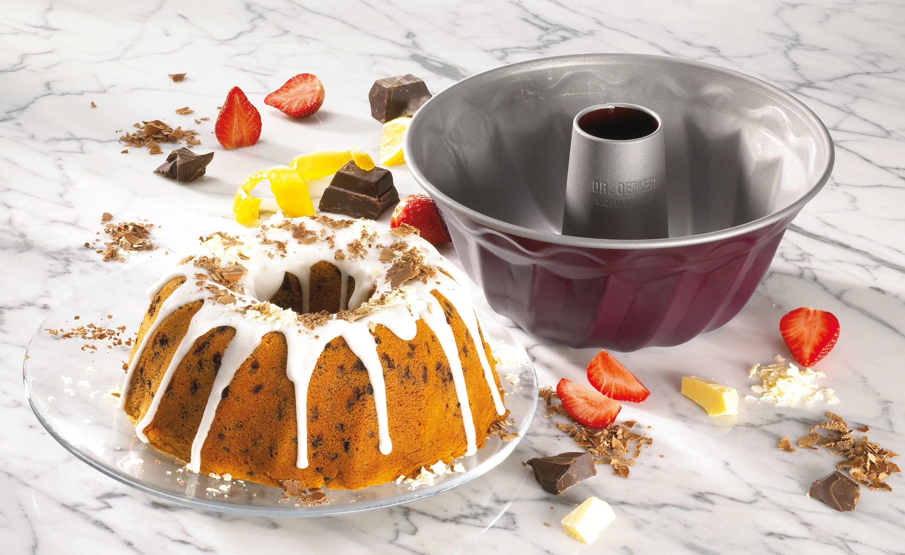 Kuchen auf Glasplatte mit Erdbeeren, Schokolade und Kuchenform. Hintergrund Marmor.