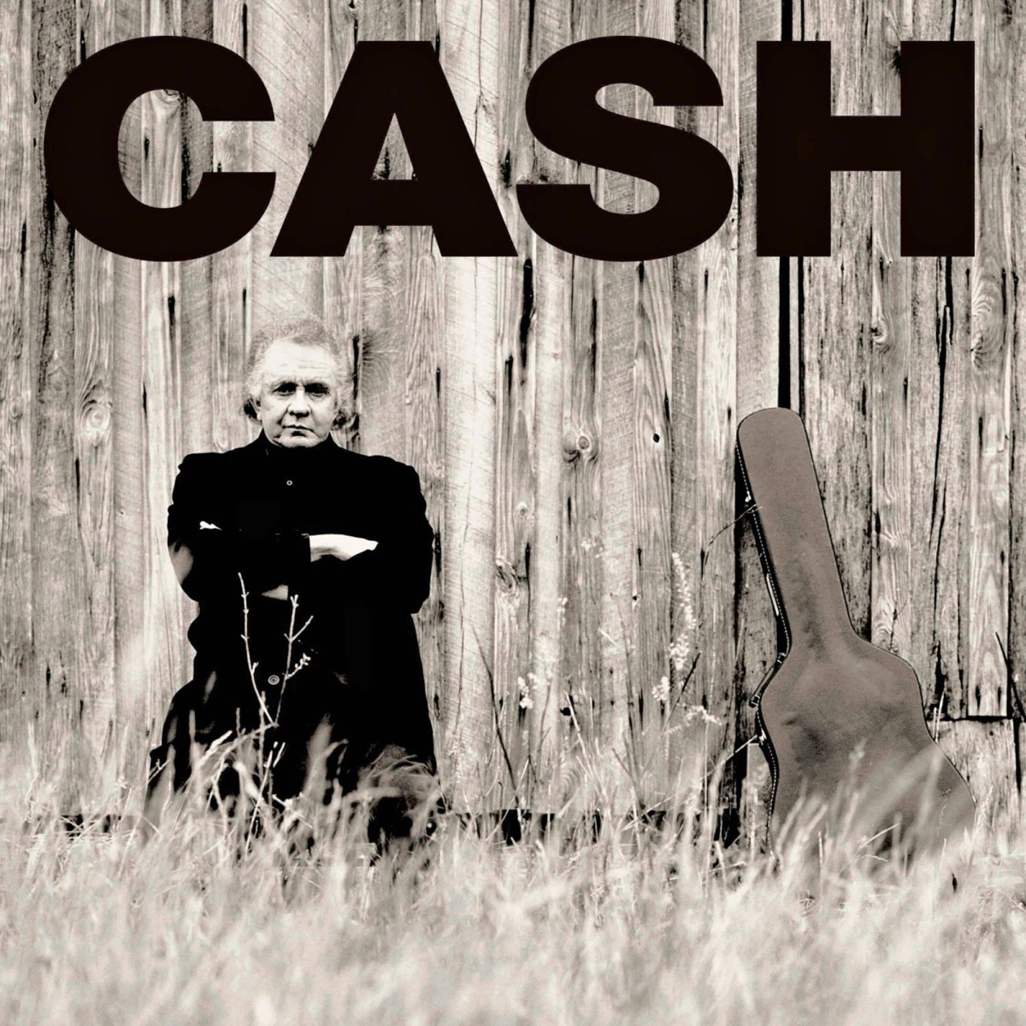 Schwarz-Weiß-Foto von Johnny Cash vor einer Holzwand mit einem Gitarrenkoffer.