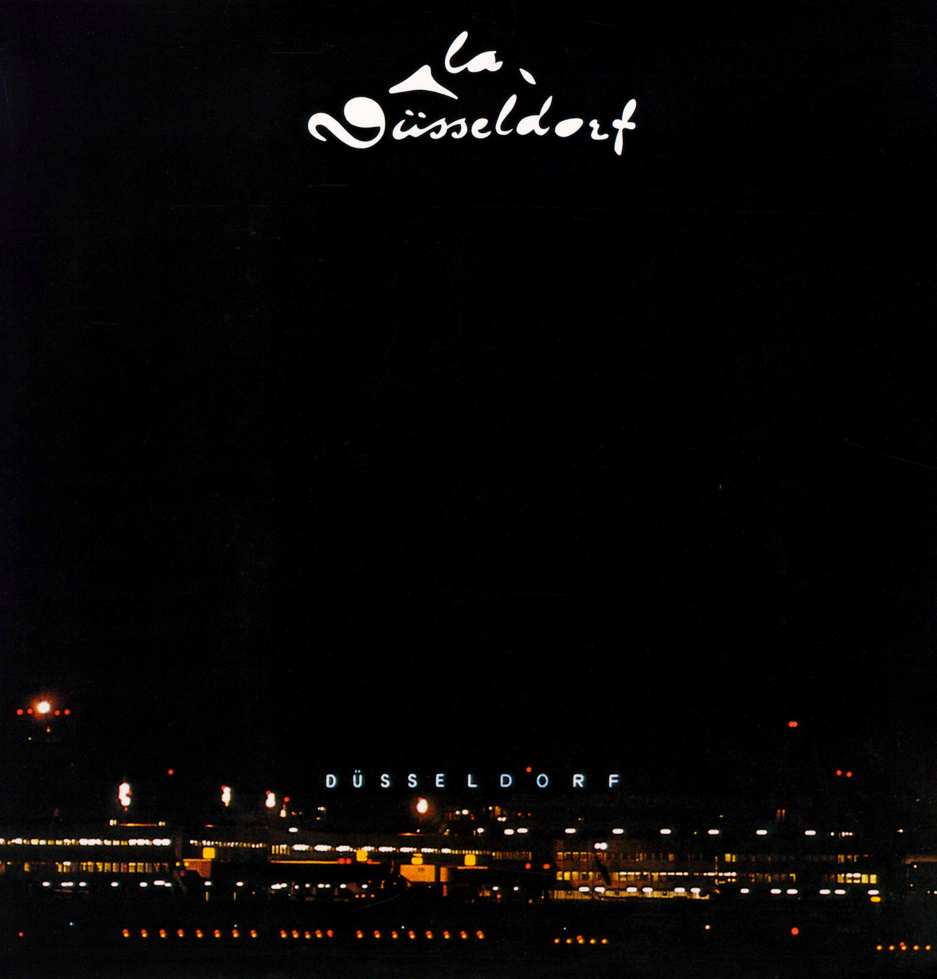 Die Nachtansicht zeigt das beleuchtete "Düsseldorf"-Logo und die Lichter eines Flughafens.