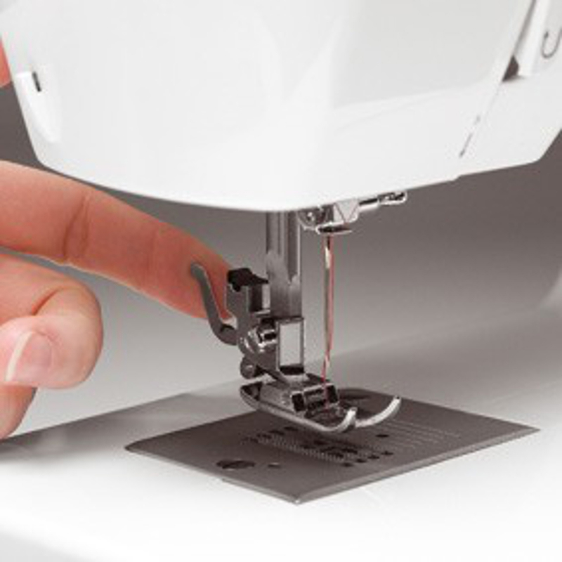 Nahaufnahme von Nadel und Nähfuß einer Nähmaschine, mit einem Finger, der den Stoff berührt.