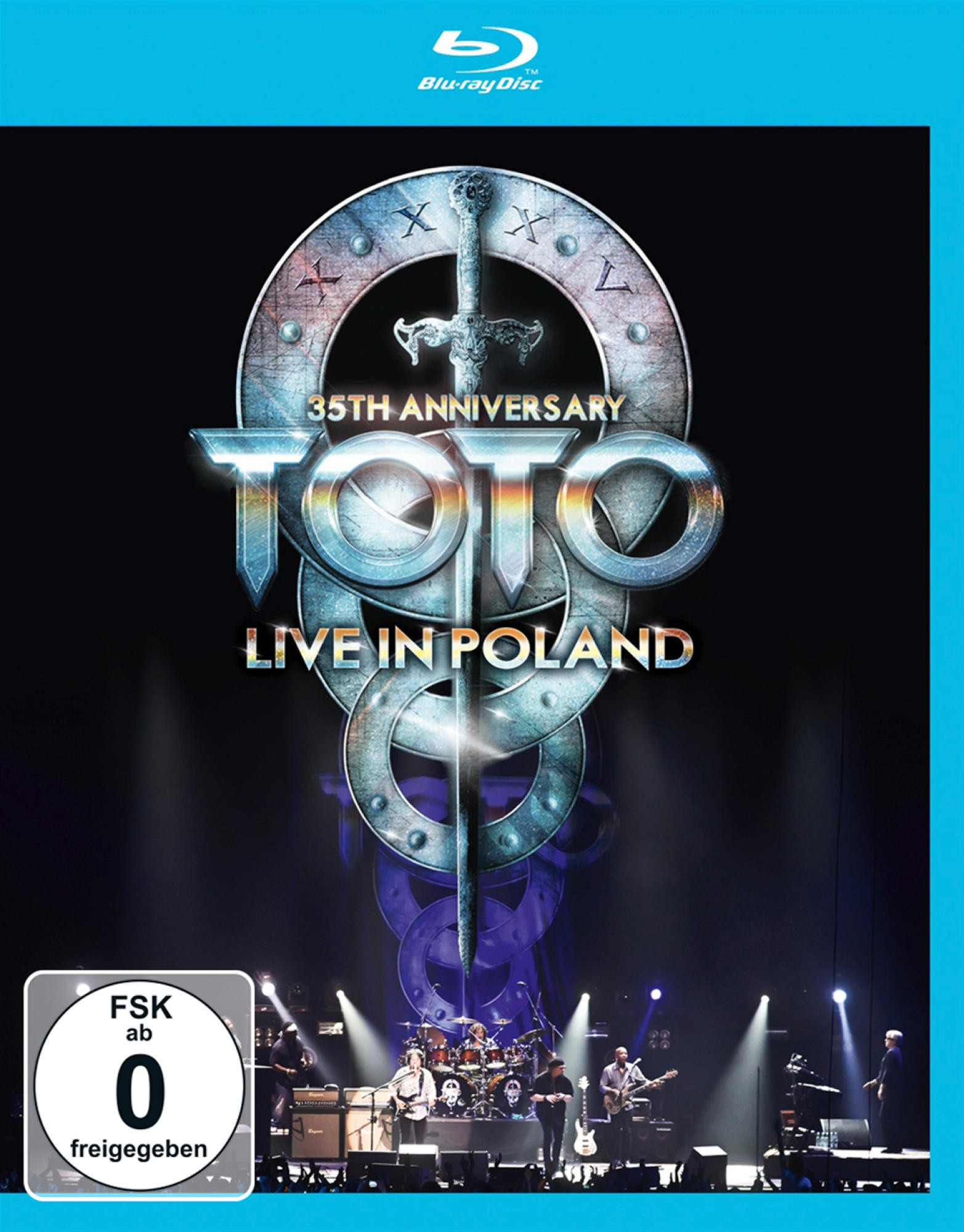 Blu-ray-Disc-Cover für Toto Live in Poland. Enthält Bandlogo, Bühne mit Bandmitgliedern, Schwertdesign und Bühne.
