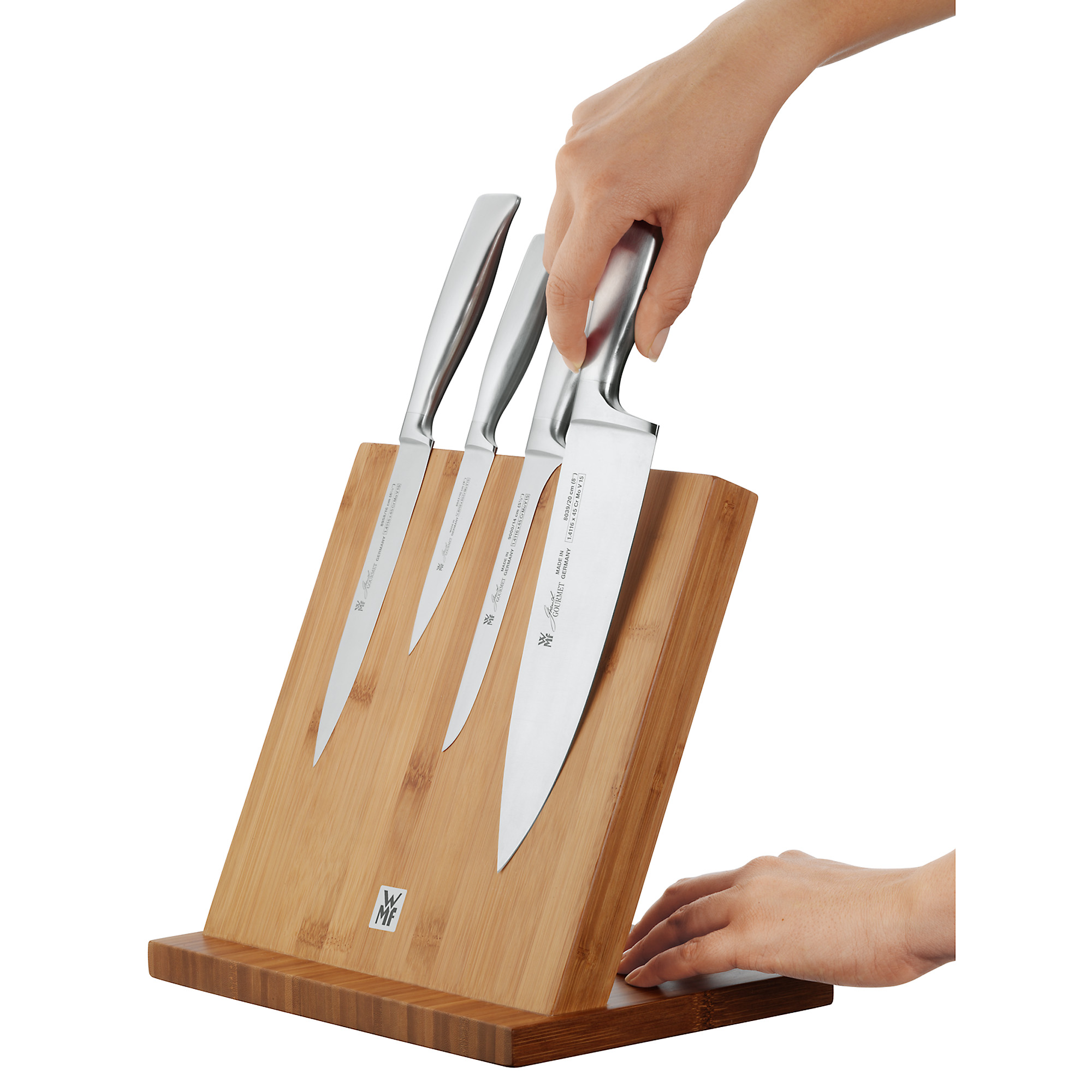 Ein Messerset auf einem Holzblock. Eine Hand hält ein Messer.