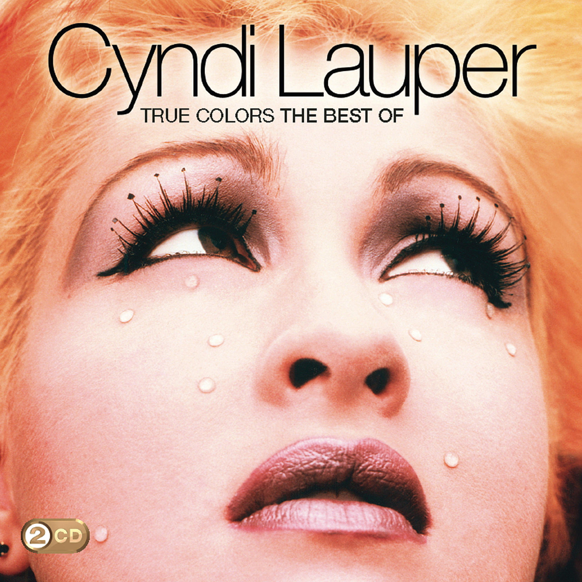 Cyndi Lauper Albumcover. Nahaufnahme ihres Gesichts, nach oben blickend mit dramatischem Augen-Make-up, umgeben von Orangetönen.
