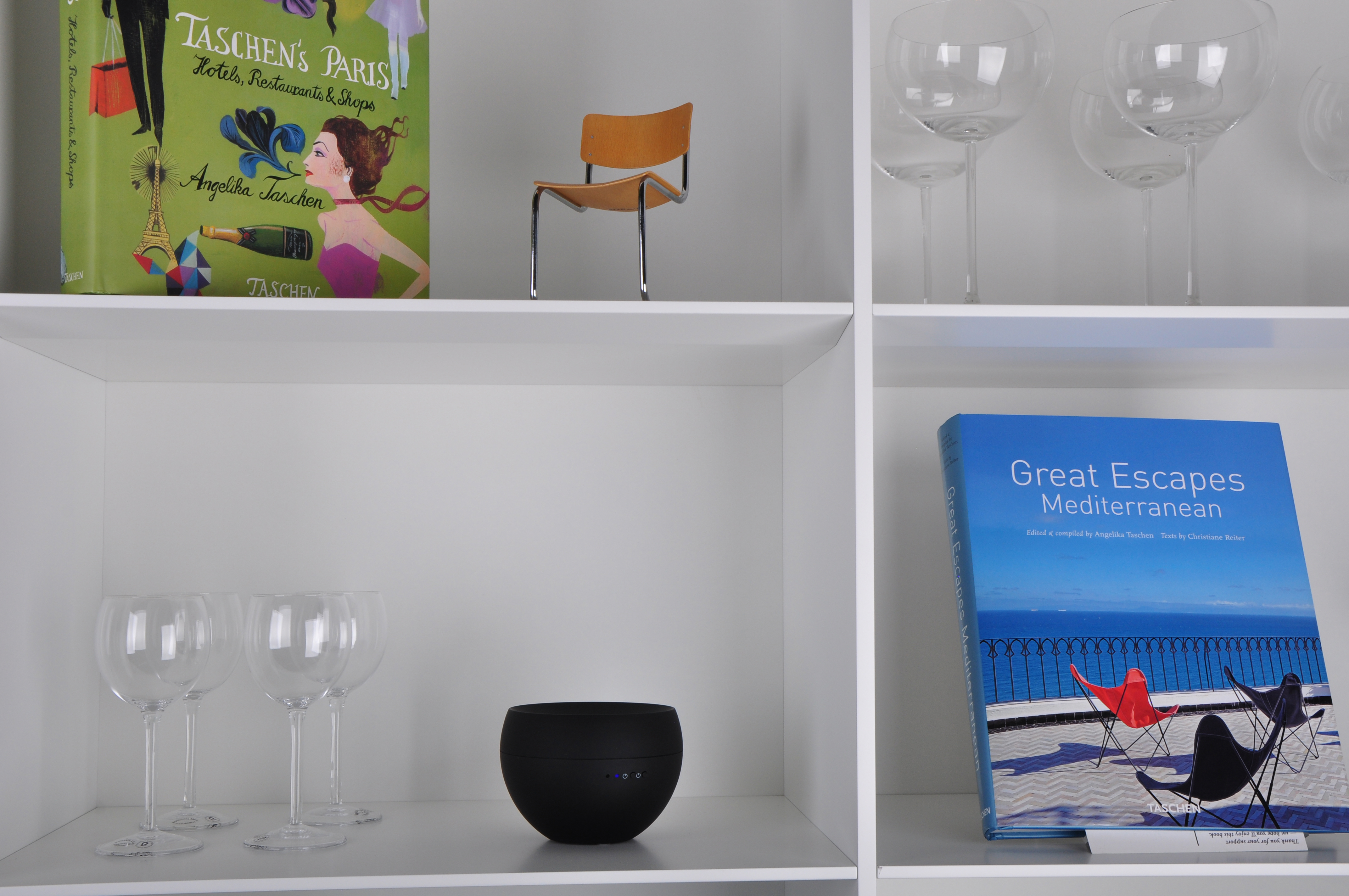 Weiße Regale mit Büchern, Weingläsern und einem schwarzen Lautsprecher.