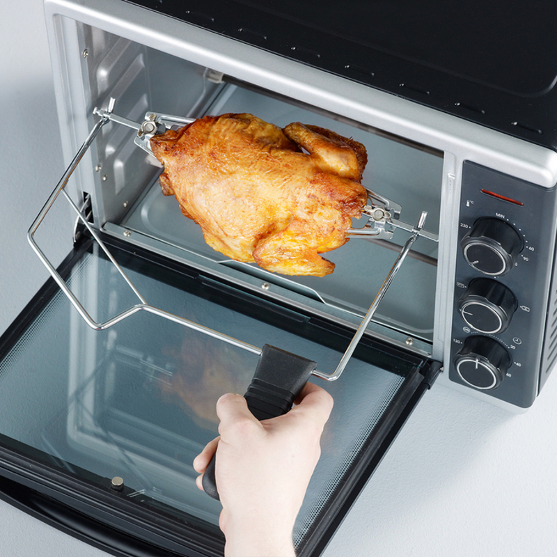 Ein Drehspießofen mit einem gebratenen Hähnchen darin. Eine Hand öffnet die Tür.