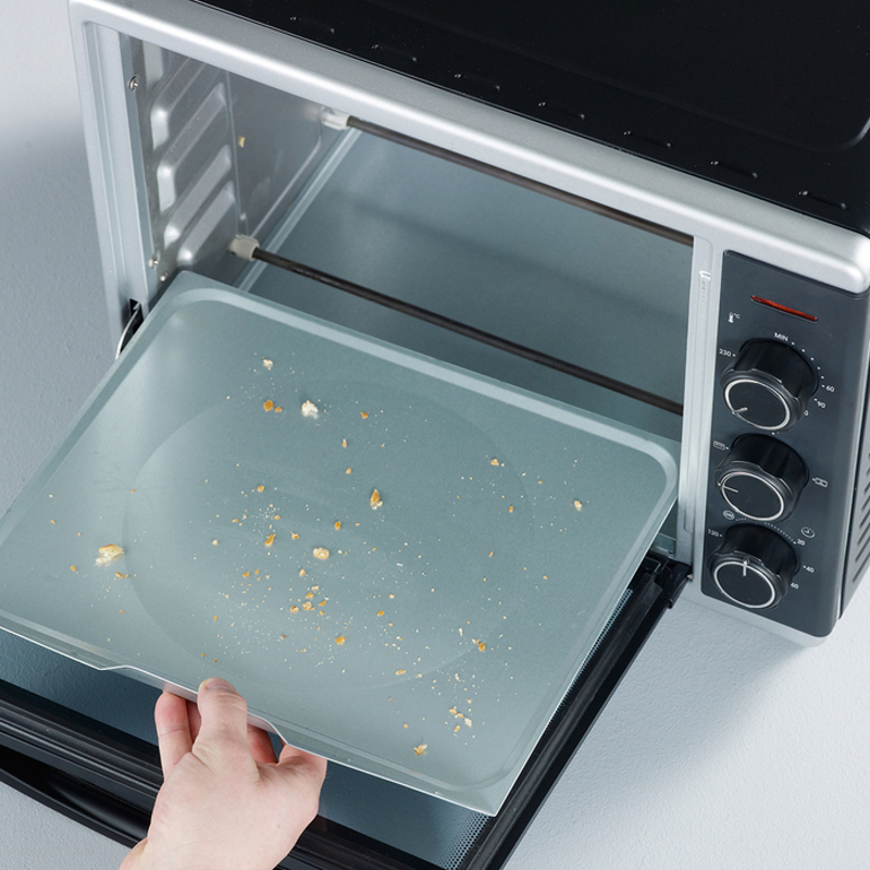 Ein offener Backofen, aus dem eine Hand ein Blech herausnimmt, Krümel auf dem Blech und dem Ofenboden sichtbar.