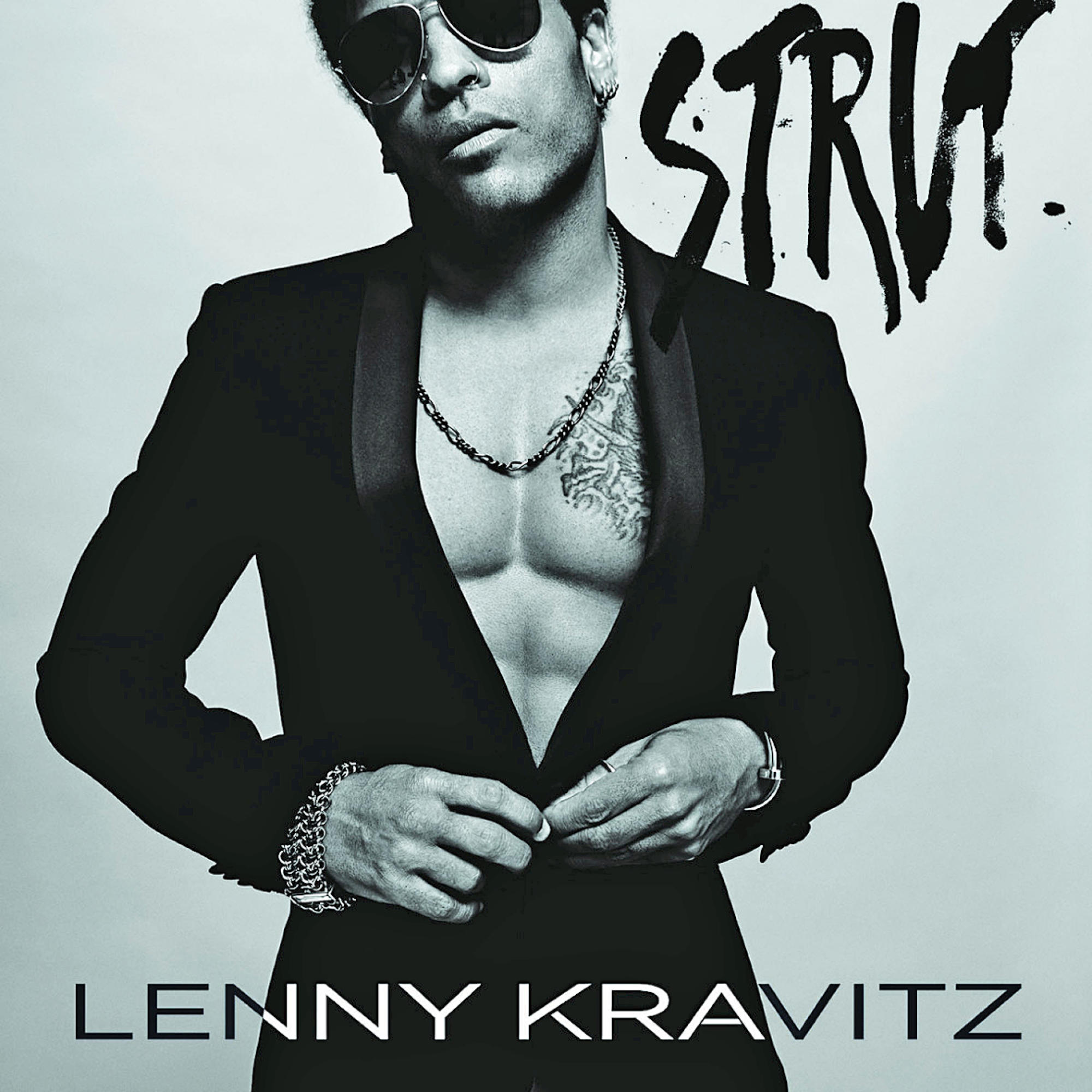 Albumcover von Lenny Kravitz in einem schwarzen Anzug, mit Tattoo und Halskette. Der Albumtitel 'Strut' ist sichtbar.