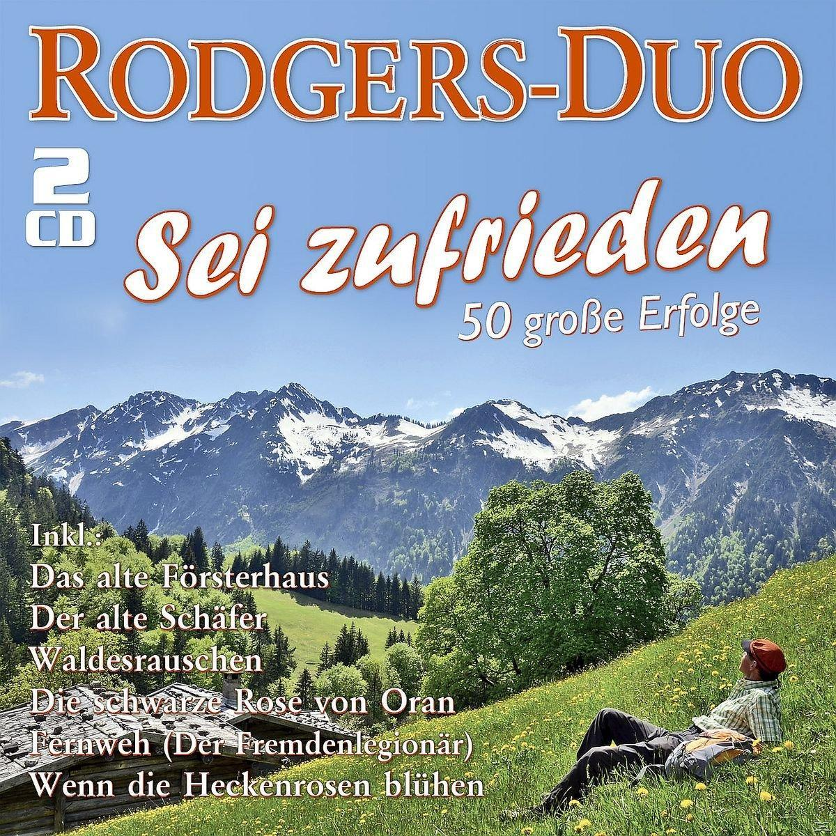 Albumcover mit Berglandschaft, Text 'Sei zufrieden'. Mann entspannt sich auf grünem Hang.