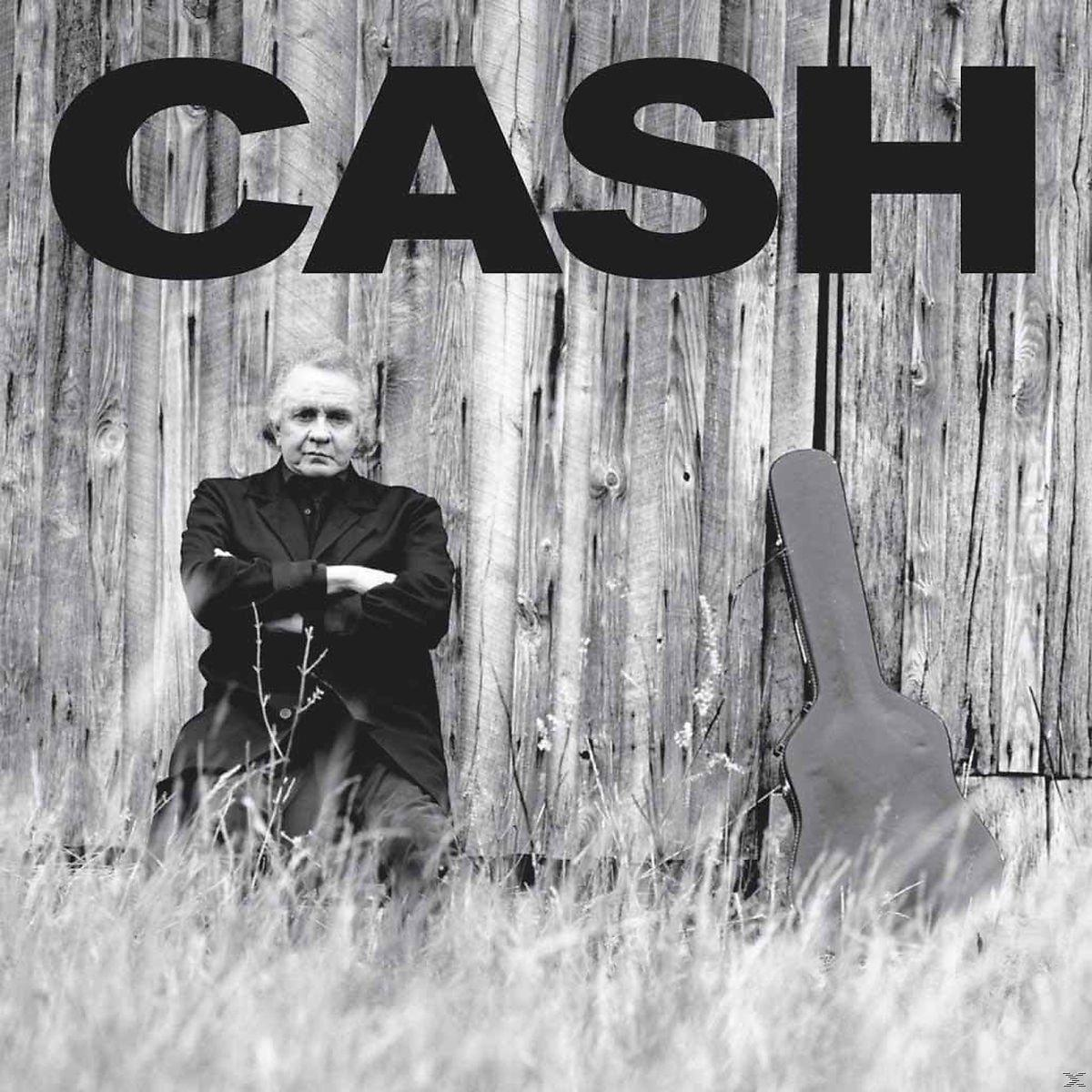 Johnny Cash steht vor einer Holzwand, mit einem Gitarrenkoffer.