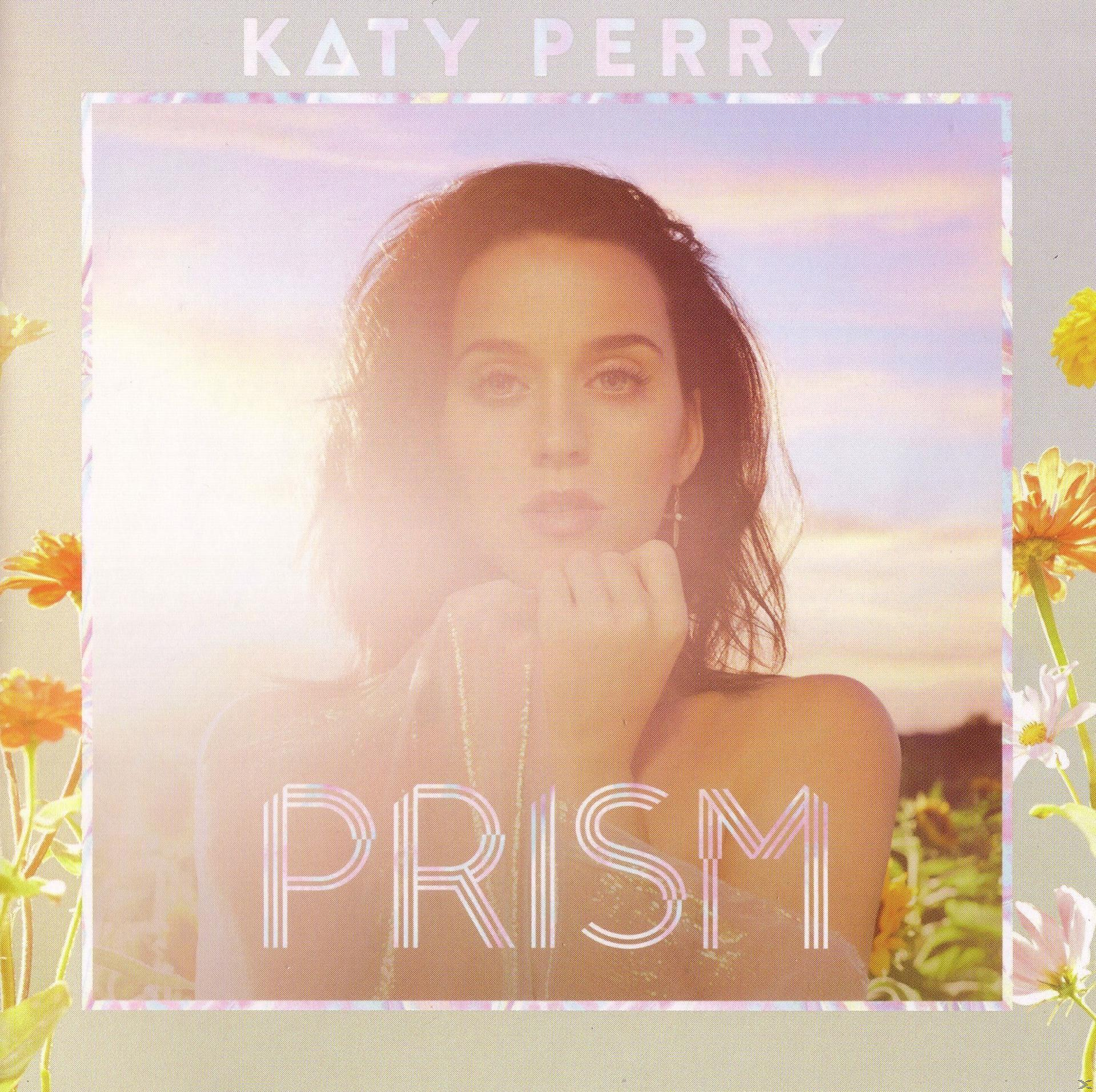 Katy Perry Albumcover: Gesicht, Titel Prism. Blumen an der Seite. Sonnenuntergang im Hintergrund.