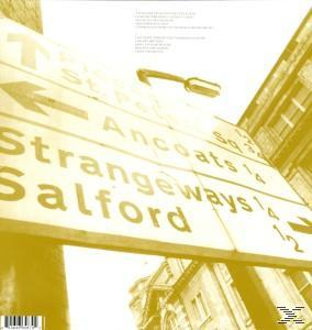 Wegweiser, gelb getönt. Wegbeschreibungen zu Orten wie Ancoats, Strangeways, Salford. Gebäude im Hintergrund.
