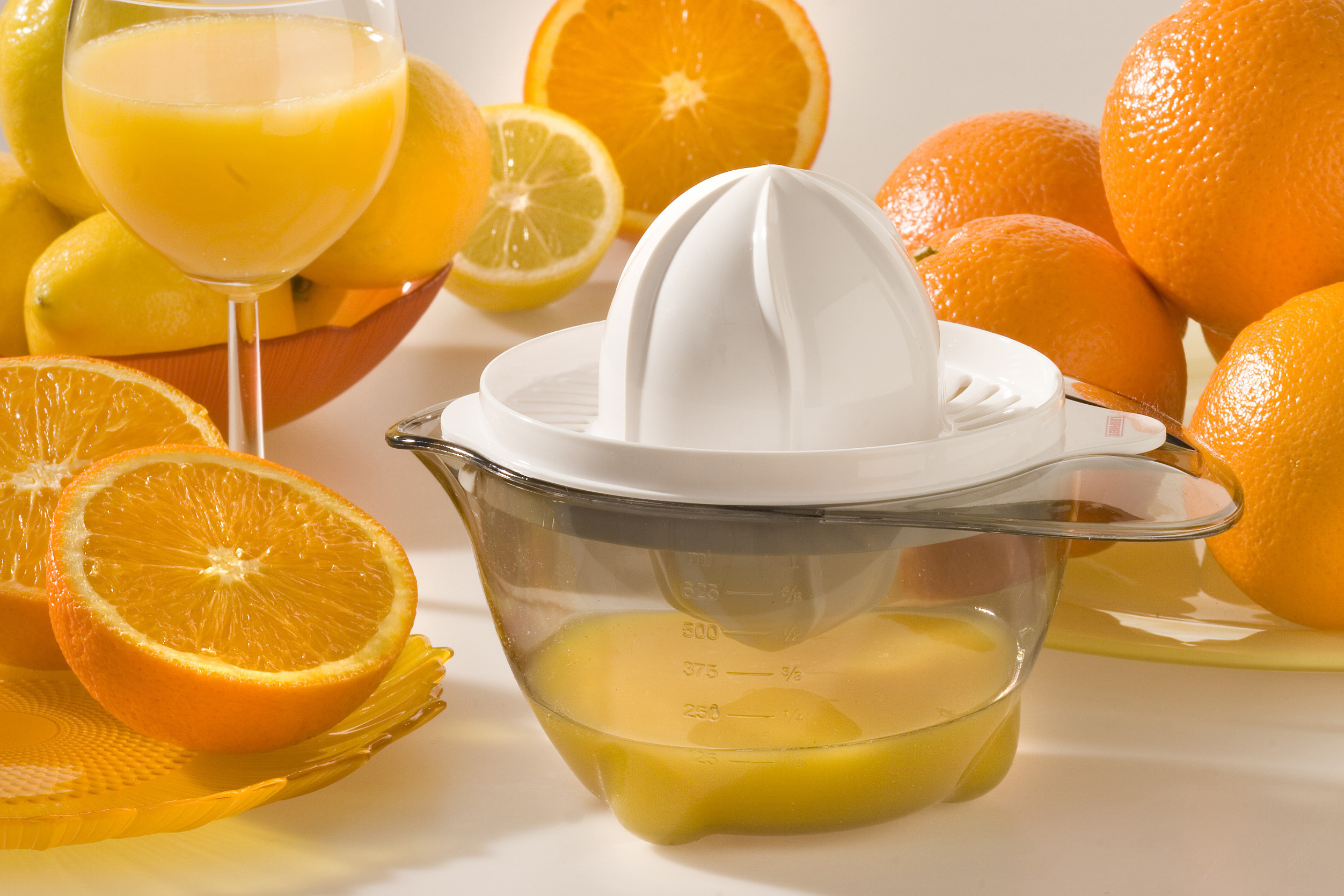 Saftpresse mit Orangen und Zitronen, mit einem Glas Saft im Hintergrund.
